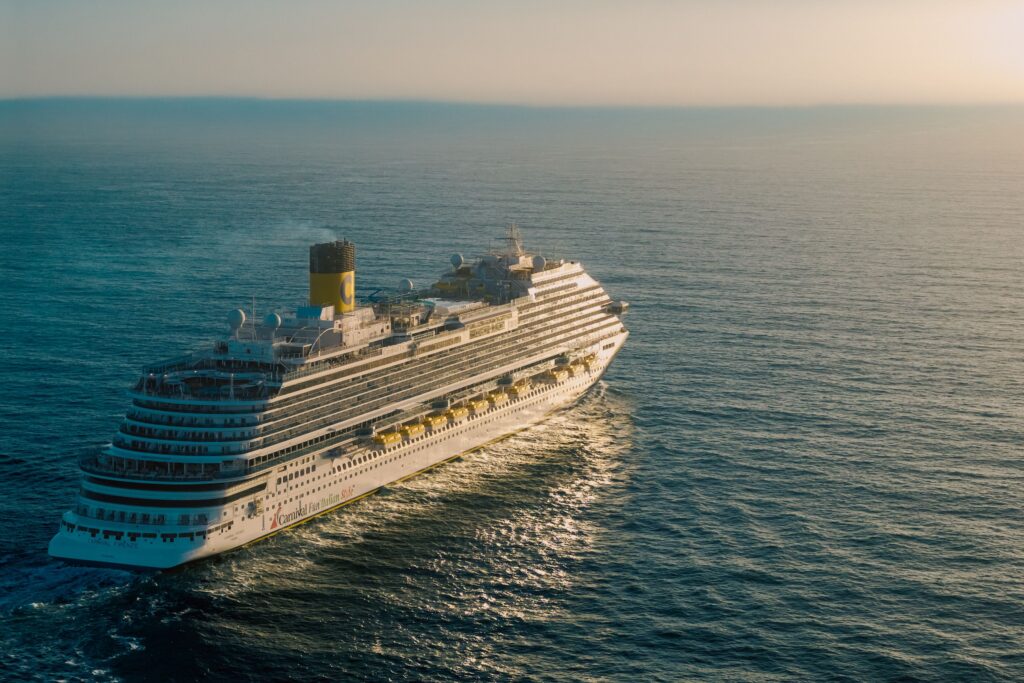 A breathtaking view of a cruise ship sailing across the ocean with the sun setting in the background.