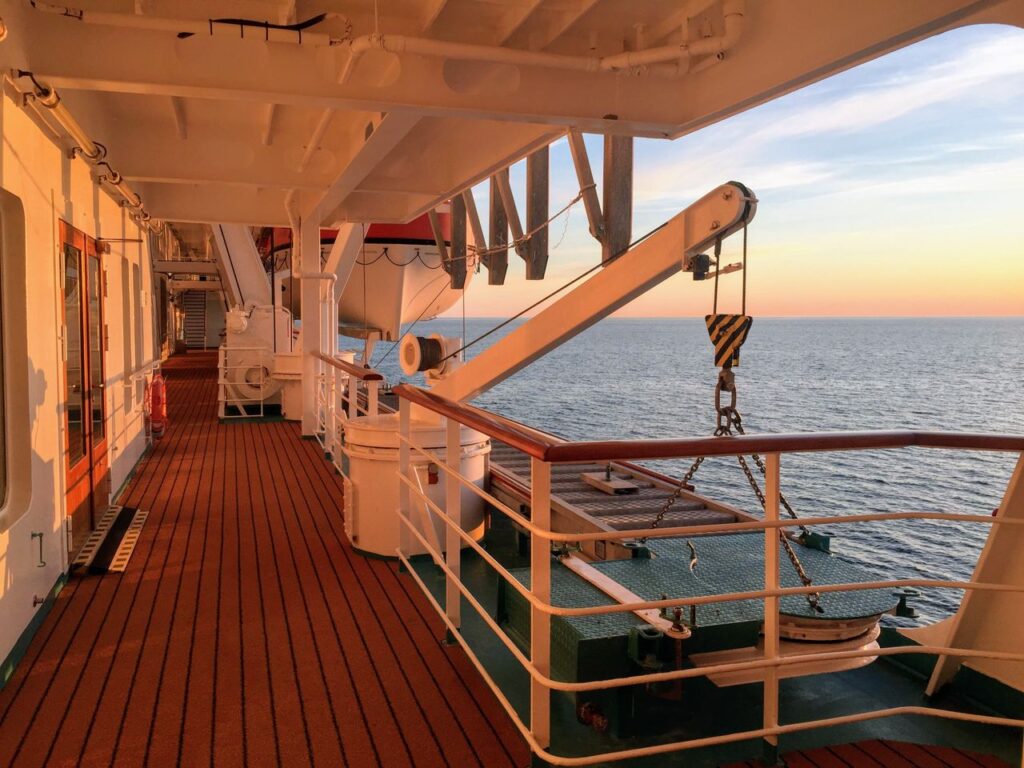 A serene view of the promenade deck on a cruise ship at sunset, overlooking the ocean.