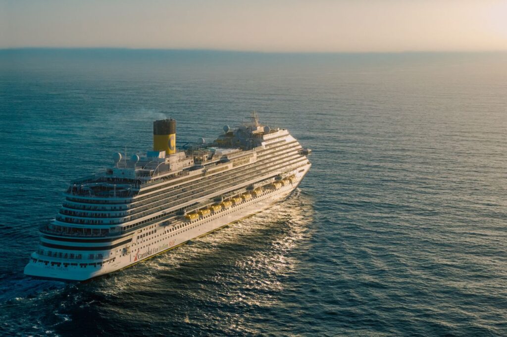 A breathtaking view of a cruise ship sailing across the ocean with the sun setting in the background.